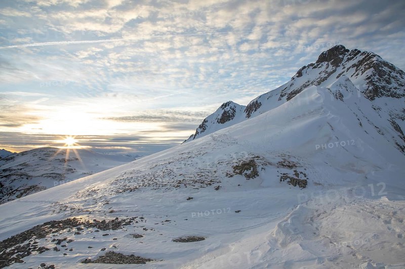 Scenic winter landscape with snow-covered mountains perfect for ski touring. The sunrise casts a warm glow over the peaks, creating a serene and majestic atmosphere