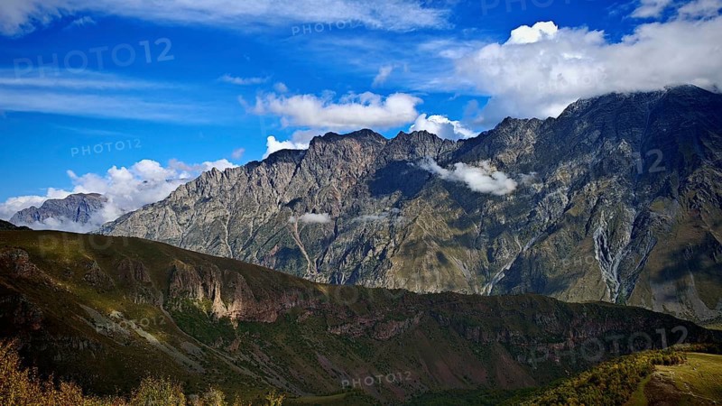 Wide mountain landscape under blue sky surrounded by clouds, Stepantsminda, Caucasus, Georgia