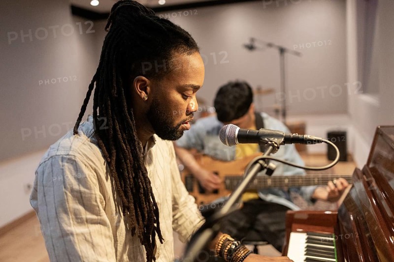 Two musicians immerse themselves in crafting music in a recording studio. One plays the piano while the other accompanies on guitar, each focused on creating harmonious melodies