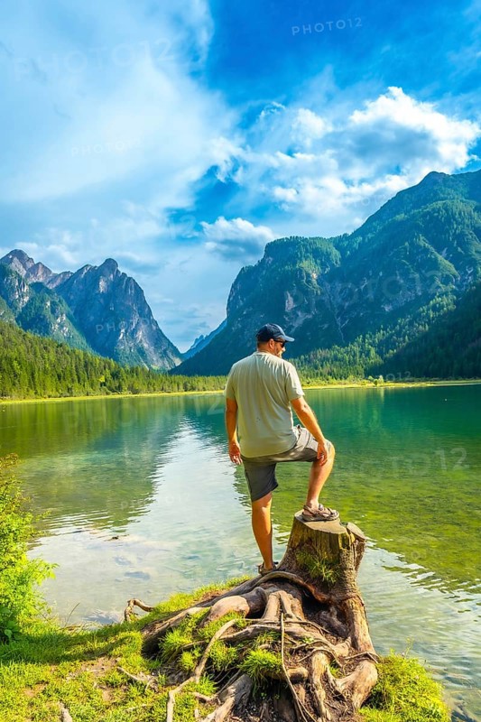 Tourist standing on a tree stump admires the breathtaking landscape of lake dobbiaco, surrounded by the majestic dolomites on a sunny summer day