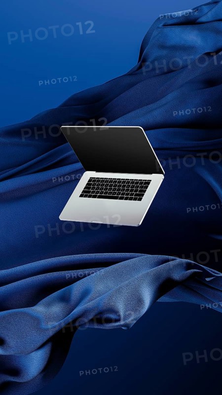 A sleek laptop is placed atop smooth fabric, showcasing its lightweight design against a rich blue backdrop