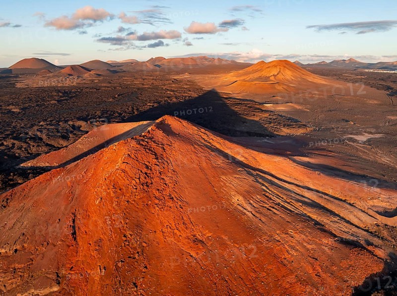 Picturesque volcanic landscape in evening light, red volcano Montaña Bermeja between lava fields, aerial view, Lanzarote, Canary Islands, Spain