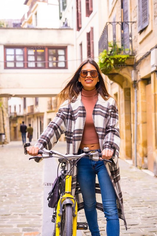Pretty latin woman with sunglasses doing bicycle sightseeing in the city through the old town. Eco tourism in spring on vacation, model smiling
