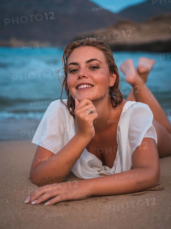 Lifestyle of a blonde Caucasian girl in a white swimsuit. Smiling in the sand after getting out of the water with the sea in the background