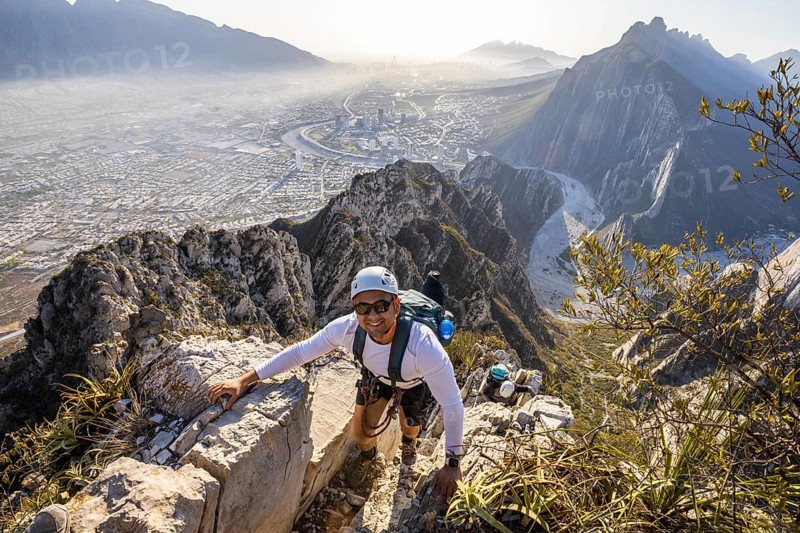 A man skillfully practices mountaineering and rappelling at Eagleâ€™s Nest in Monterrey, Mexico, with a breathtaking cityscape view in the backdrop on a clear day
