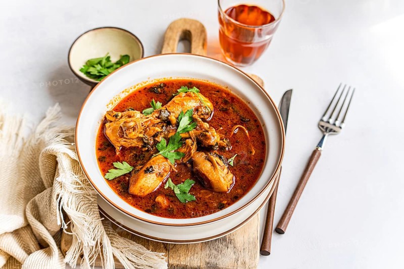 A hearty bowl of Georgian chicken stew, chakhokhbili, immersed in rich tomato sauce with paprika and fresh herbs like coriander. Perfect for a flavorful meal experience