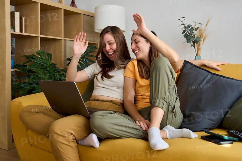 A cheerful lesbian couple relaxes on a cozy yellow sofa, smiling and enjoying quality time together Showcasing love and happiness in an inclusive LGBTQIA+ setting