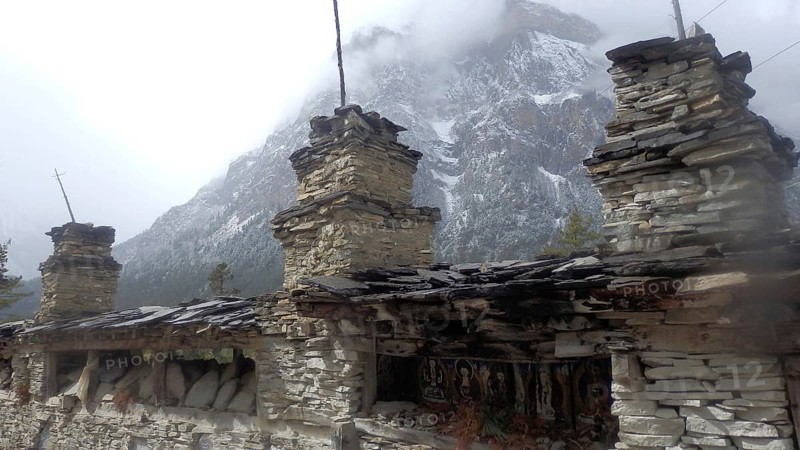 Stone structures in front of a misty mountain landscape, cold and calm atmosphere, trekking at Annapurna Circuit, Manang, Nepal