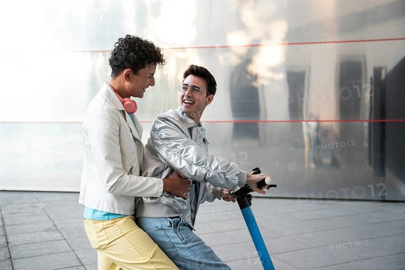 A cheerful gay couple enjoying a scooter ride together on a sunny day, wearing casual outfits. Their happiness and connection are evident as they share this fun experience