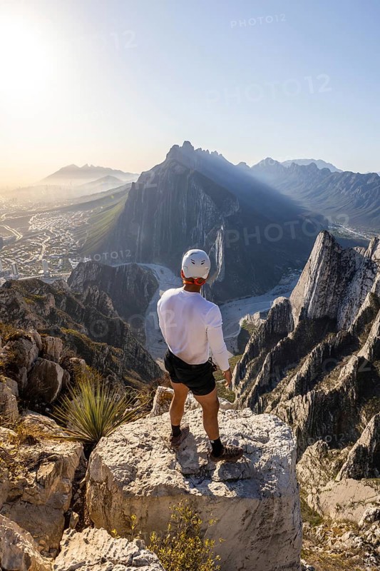 A man stands on a rocky peak at Eagle's Nest in Monterrey, Mexico, taking in the breathtaking view after a day of mountaineering and rappelling. The city and mountains stretch below
