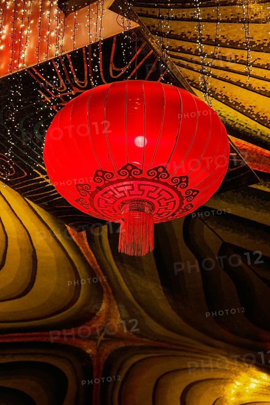 A vivid red lantern adorned with intricate patterns hangs in the festive atmosphere of a Taoist and Chinese Buddhist temple in Macau, illuminated by twinkling lights