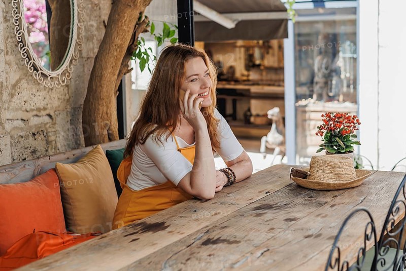 A mature woman, wearing an orange and yellow outfit, enjoys a phone call during her vacation in an old city in Turkey, showcasing a relaxed travel moment