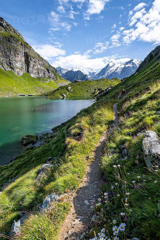 Mountaineer on a hiking trail at a mountain lake with a view of glaciated mountain peaks, Lac du Louvie with summit Grand Combine, Valais Alps, Val de Bagnes, Valais, Switzerland