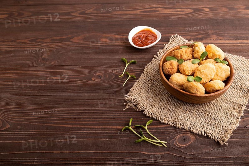 Fried crispy Chicken Nuggets with ketchup, microgreen on brown wooden background and linen textile. side view, copy space