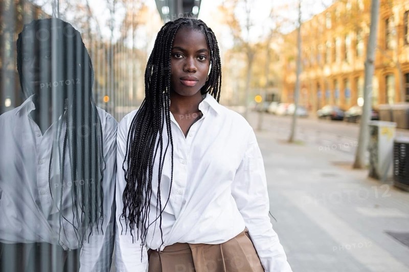 An African American businesswoman with braids is featured standing outdoors, wearing a formal white shirt and khaki trousers, with a focused expression