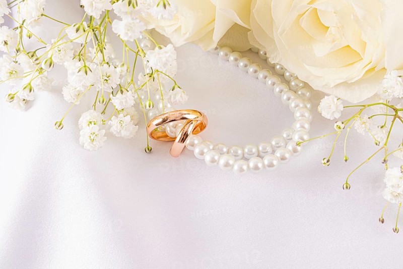 Elegant wedding rings lie nestled among delicate white roses and dainty baby's breath. The sophisticated arrangement exudes romance and timeless beauty, perfect for a wedding theme