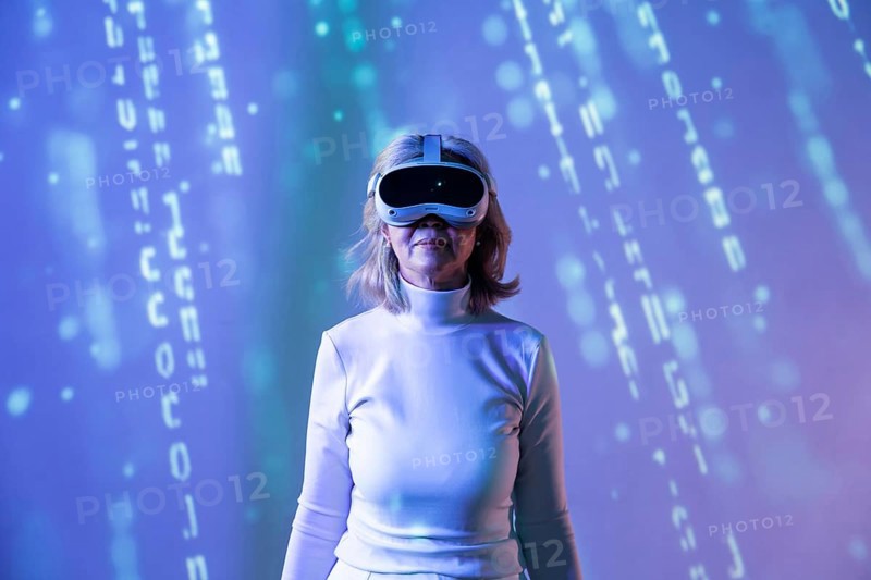 An elderly Asian woman, wearing a VR headset, explores the metaverse, surrounded by digital graphics. She experiences virtual reality in a futuristic setting with blue tones