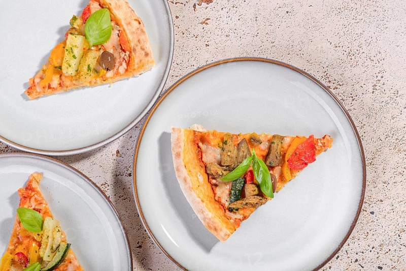 Delicious vegetarian pizza slices topped with vibrant zucchini, eggplant, olives, and basil. Served on ceramic plates, this savory meal is perfect for lunch or dinner