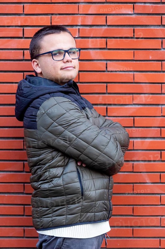 A young man with an intellectual disability stands confidently with arms crossed against a brick wall