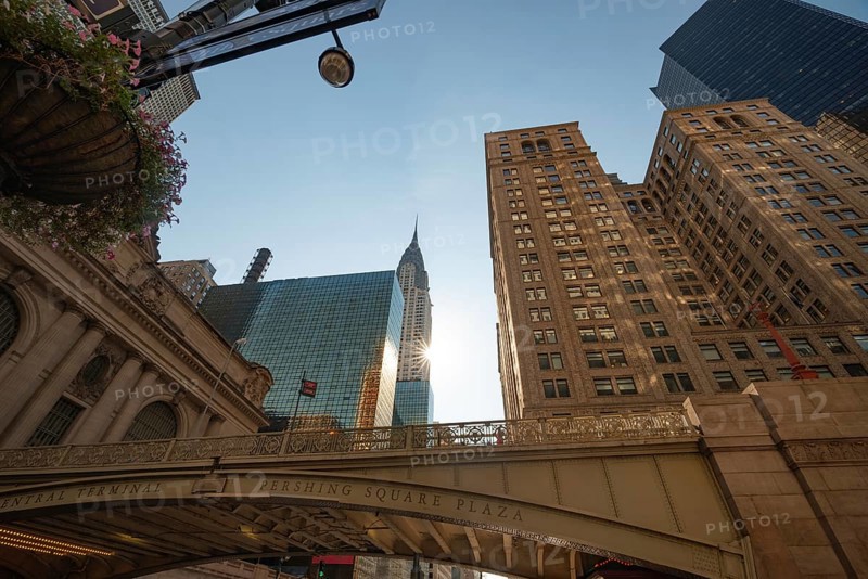From below the morning view of Pershing Square Plaza in front of Grand Central Terminal with the iconic Chrysler Building and modern skyscrapers in Manhattan, New York City. The soft sunlight enhances the majestic urban scenery