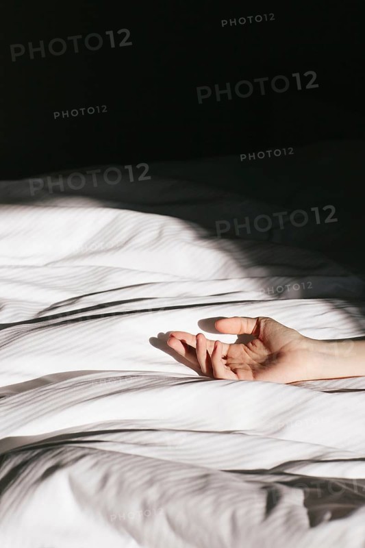 A serene hotel room captured at dawn, where soft morning light filters through, casting gentle shadows on a crisp white bed. An outstretched hand adds a touch of mystery