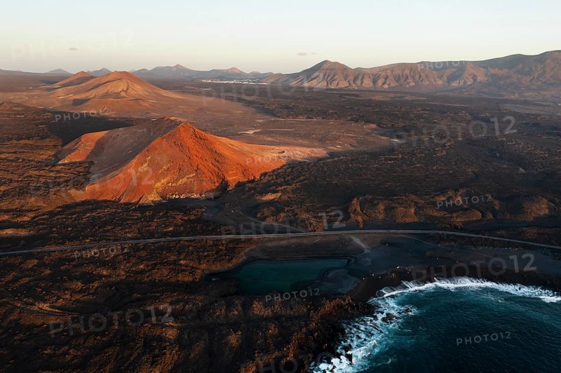 Aerial shot showcasing the stunning juxtaposition of Timanfaya national park and Los Hervideros against the dark volcanic terrain, under the golden hour light