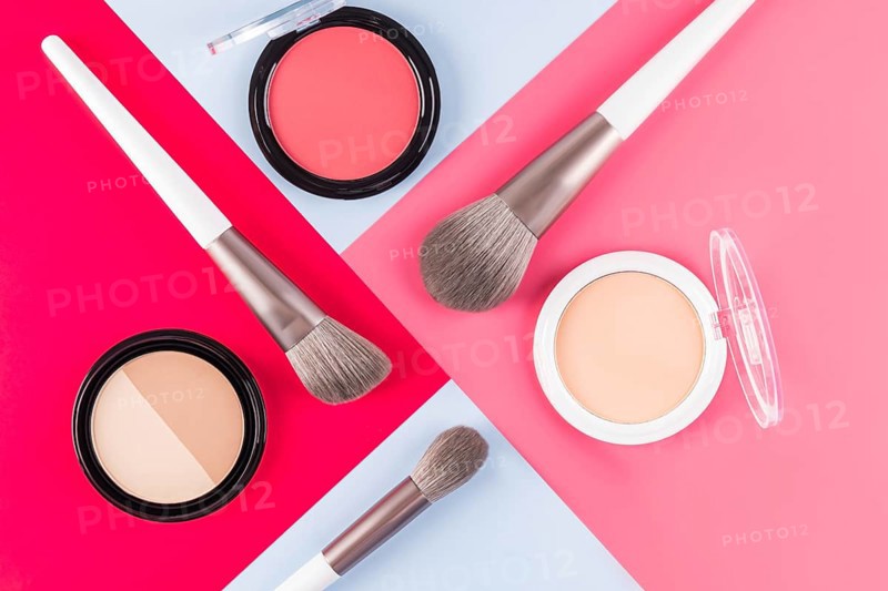 Aesthetic arrangement of makeup brushes and powder compacts on contrasting red, pink and blue surfaces. Perfect for beauty, fashion, and cosmetic themed designs