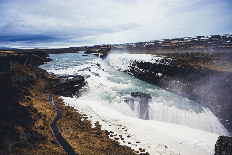 Stunning view of Gullfoss waterfall, cascading powerfully over rugged cliffs. The icy landscape and flowing water create a mesmerizing natural spectacle in Iceland