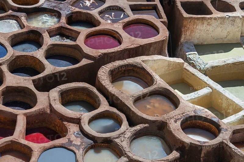 Aerial view of traditional leather tanning pits filled with vibrant dye baths in warm sunlight in Fez, Morocco. The ancient artistry showcases a stunning array of colors and textures