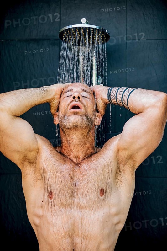 A man stands under a rainfall shower head, enjoying the refreshing flow of water. With closed eyes and relaxed expression, he epitomizes the essence of relaxation and hygiene