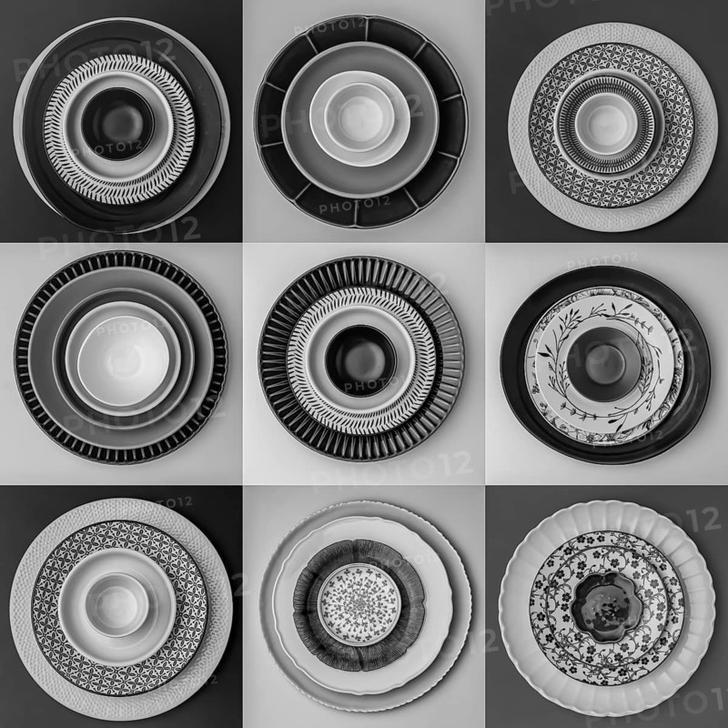 Monochrome plates and bowls with diverse geometric patterns form a striking arrangement in a grid. Each setting showcases intricate design and texture