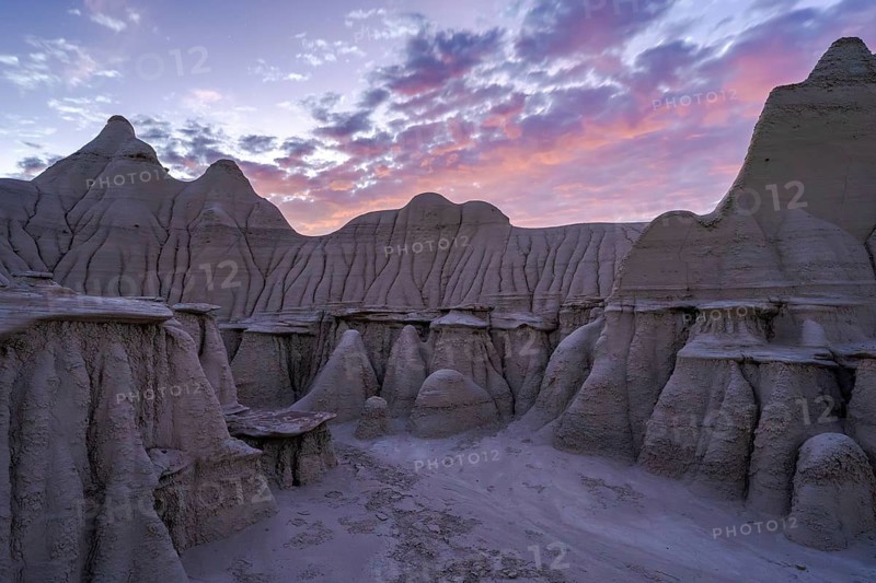 A breathtaking landscape view of the Bisti/De-Na-Zin Wilderness in New Mexico, showcasing striking eroded rock formations under a vibrant twilight sky