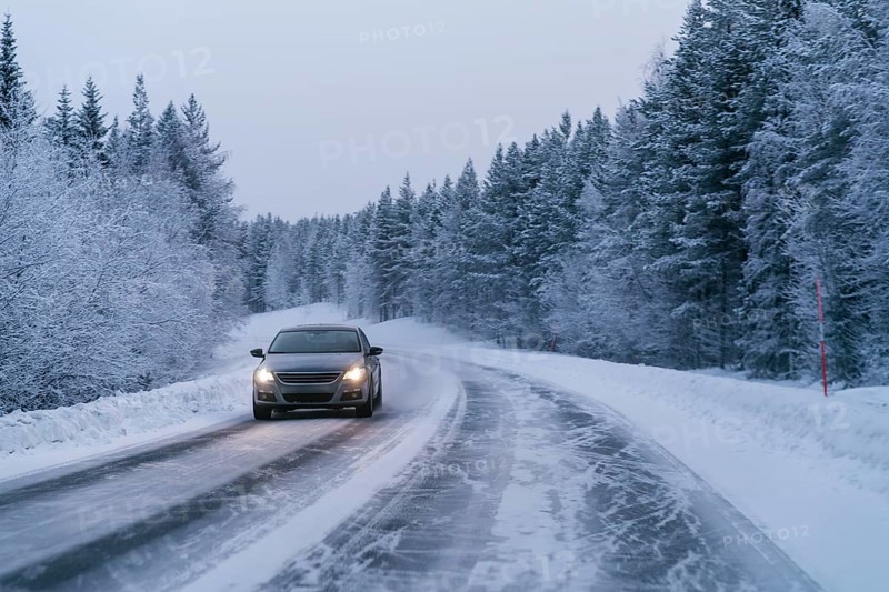A car drives along a snow-covered road, flanked by dense, snow-laden trees in the serene Swedish Lapland landscape, capturing the essence of winter driving