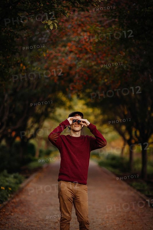 A man in a red sweater looks through binoculars amidst vibrant autumn foliage in a scenic park pathway in Quebec, Canada, capturing the essence of fall's beauty