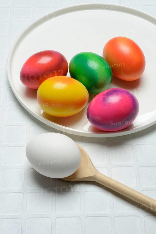 Coloured eggs on a plate and uncoloured eggs on a spoon, Easter celebration