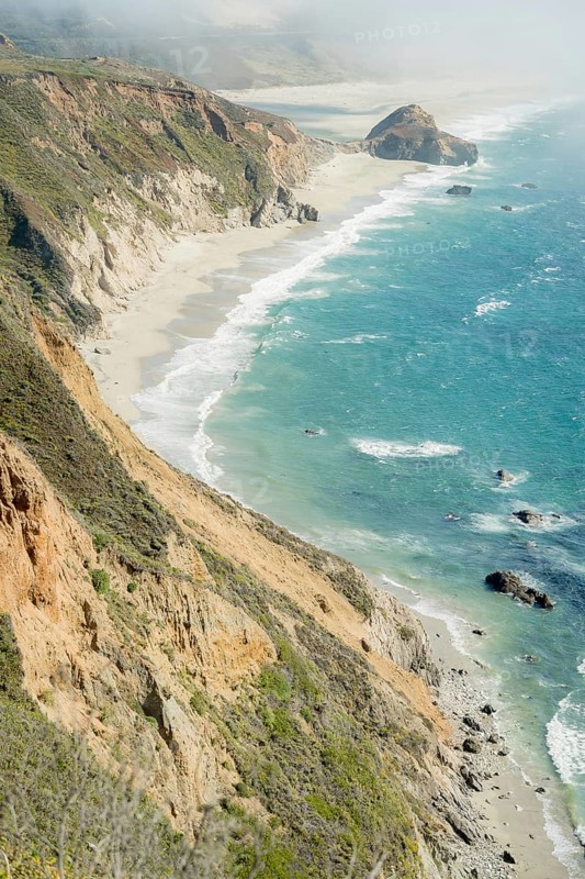 The dramatic Big Sur coastline features steep cliffs and vibrant ocean waves crashing against the shore, creating a stunning view of California's natural beauty
