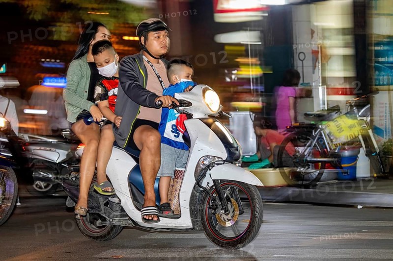 A family rides a scooter through a busy city street at night, people on scooters drive through the streets of Hanoi Vietnam