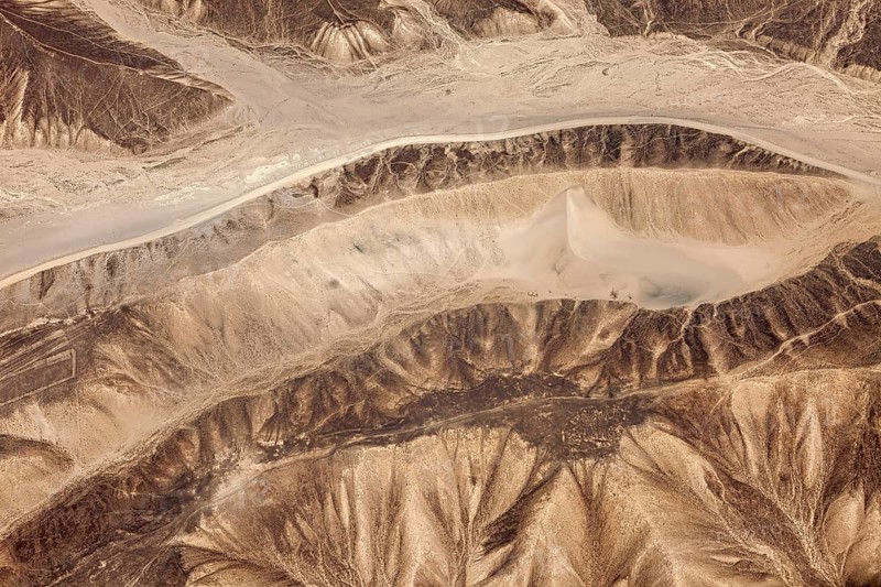 Aerial view of a dry, mountainous desert landscape with sandy shades of brown, the landscape and desert near Nasca in the Andes of Peru