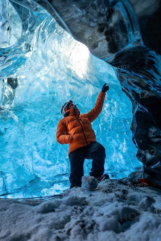 A man in an orange jacket in a glacier cave in Iceland in winter
