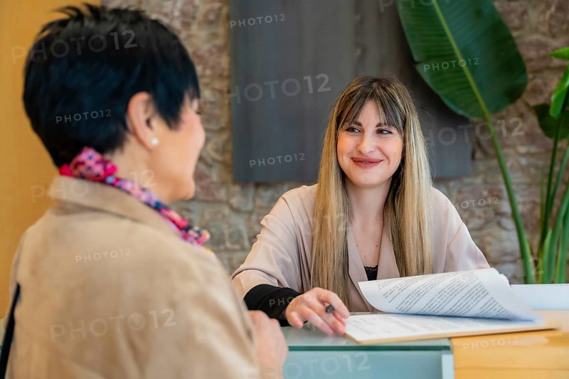 Client having a consultation with a smiling blonde receptionist, filling out documents and discussing services at a modern aesthetic beauty center reception desk