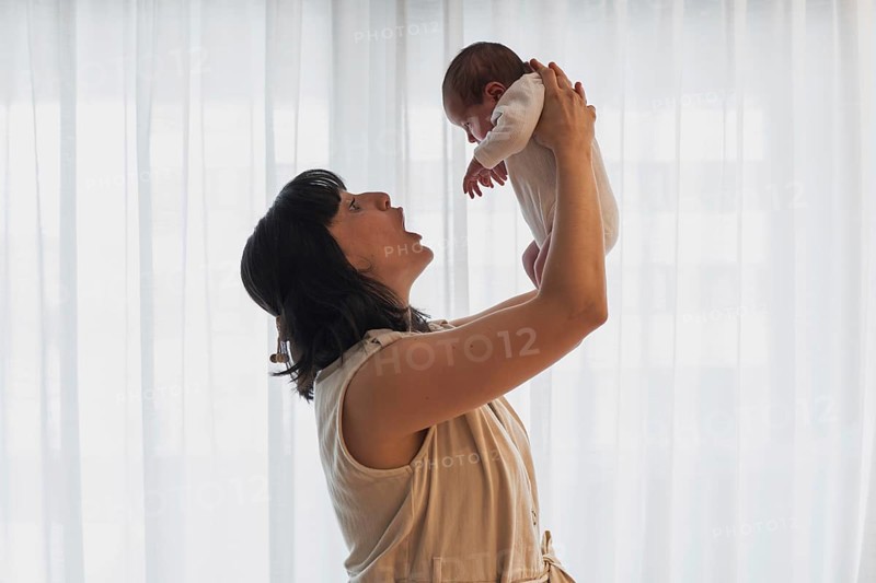A joyful young mother holds her newborn baby lovingly in a softly lit room. This tender moment captures the essence of family love and the beginning of a new journey