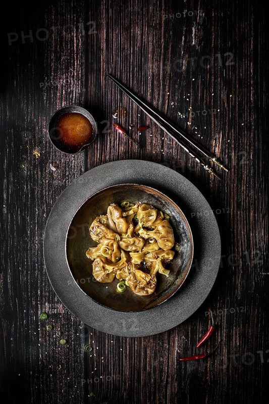 View from above of a plate of chili wontons on a wooden table next to chopsticks