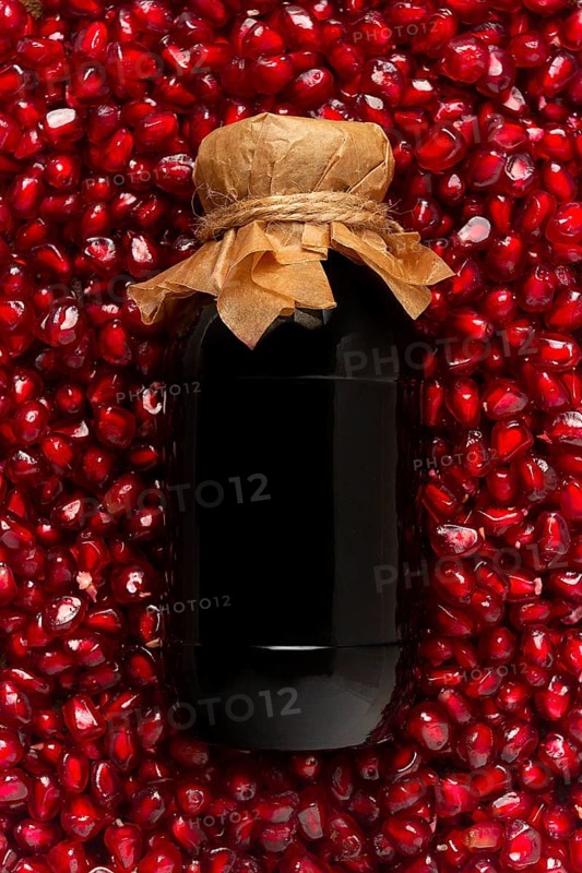 Pomegranate sauce in a bottle, top view, in pomegranate seeds, food background, vertical, no people