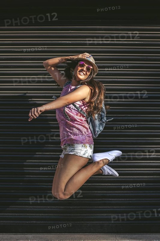 A young woman in sunglasses and a hat jumps joyfully against a dark urban background, embodying freedom and happiness. Perfect for lifestyle and youth-related projects