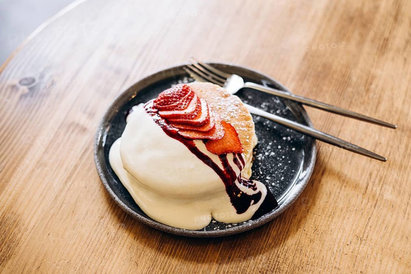 Fluffy japanese pancakes topped with fresh strawberries, a drizzle of cream, and berry sauce. Served on a dark plate, this inviting breakfast dish is perfect for food lovers