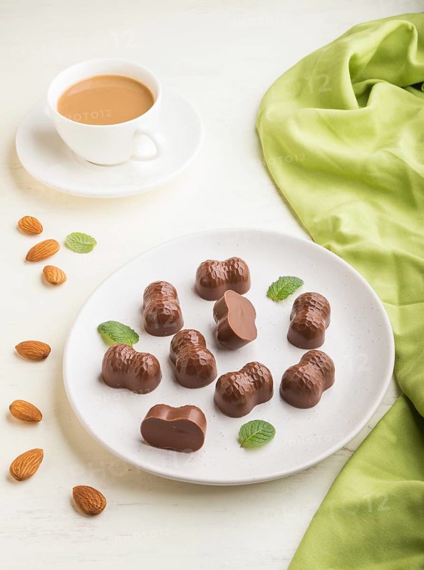 Chocolate candies with almonds and a cup of coffee on a white wooden background and green textile. side view, close up