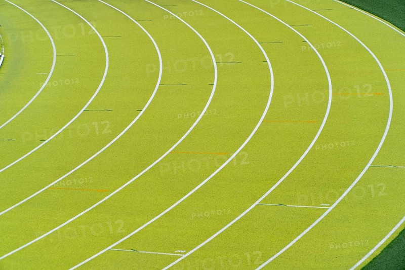 A vibrant aerial shot of a freshly marked bright green running track at an outdoor athletics stadium featuring distinctive white lines and curves