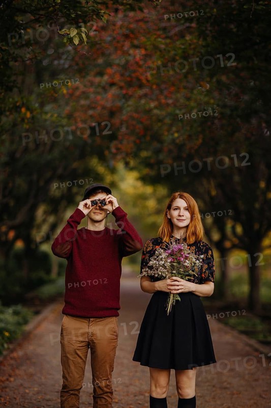 A couple enjoying a beautiful fall day in Quebec, Canada. The woman holds a bouquet of wildflowers, while the man looks through binoculars, surrounded by autumn foliage