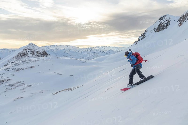 A snowboarder rides down a pristine snowy slope, surrounded by stunning alpine peaks under a soft, cloudy sky, highlighting the adventure and beauty of nature