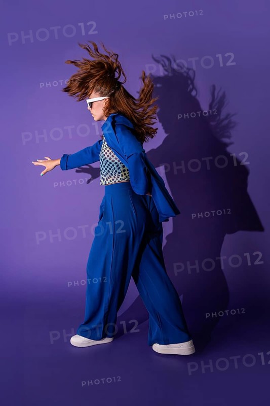 A young woman dances energetically against a vibrant purple background. Her dynamic pose and flowing hair capture a sense of freedom and movement, showcasing vibrant energy